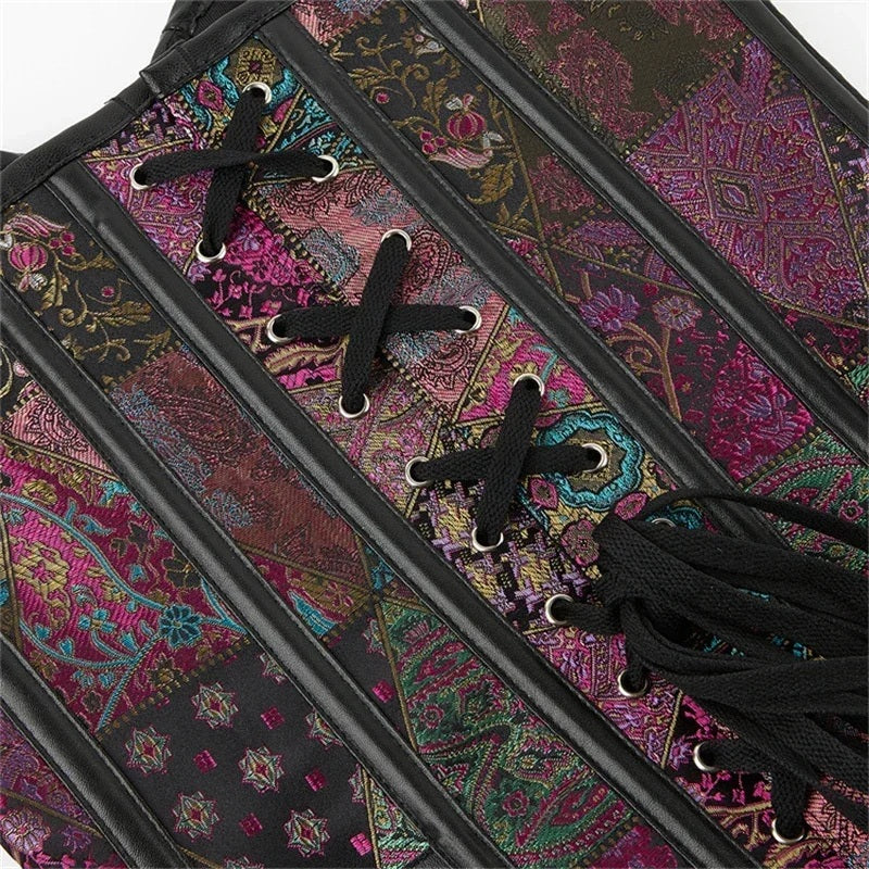 Close-up of a patchwork corset top with colorful paisley and floral fabric panels, black faux-leather trim, and black laces threaded through silver eyelets.