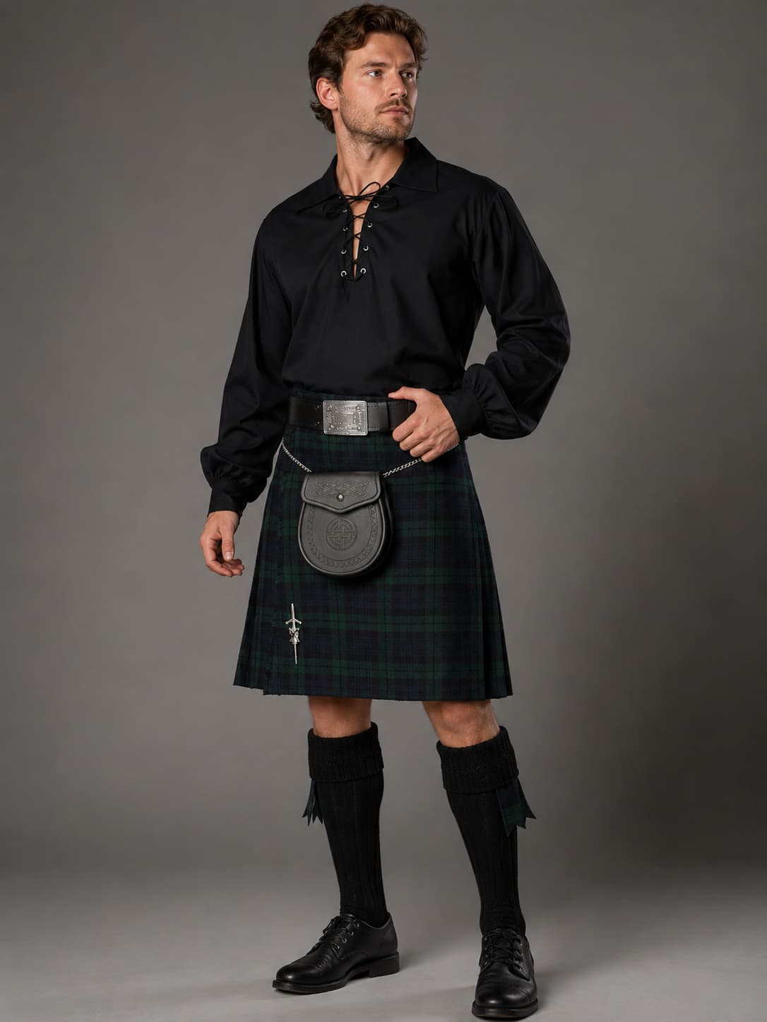Man wearing a black shirt, green kilt, and black shoes against a gray background