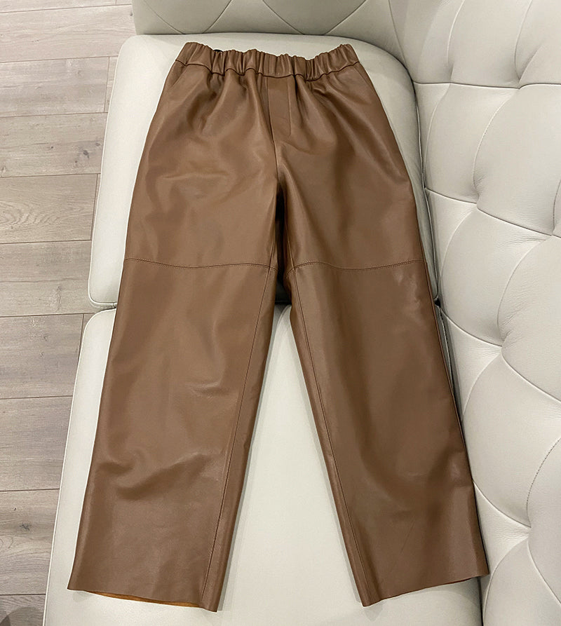 Brown leather pants on a white cushioned chair with a wooden floor background