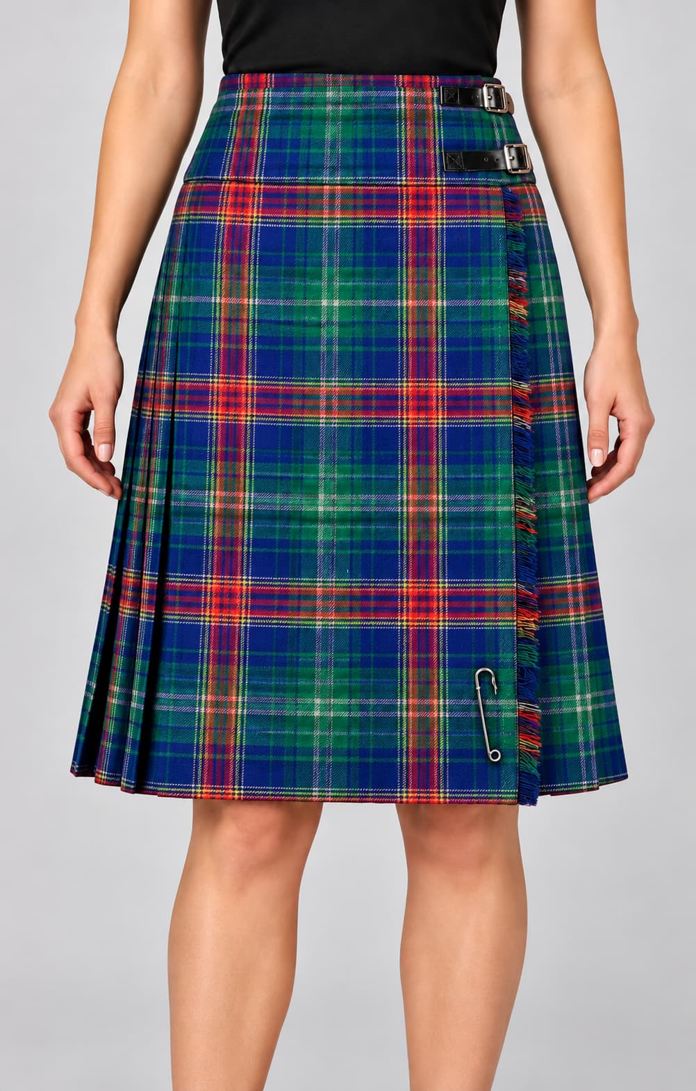 A woman wearing a pleated kilt skirt in a blue, green, red, and yellow tartan plaid pattern, featuring a black belt and a silver safety pin detail, shown against a solid gray background.