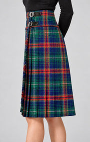 A high-waisted pleated kilt in a classic tartan plaid pattern of green, blue, red, and yellow, featuring a double-buckle waistband, shown on a model against a neutral gray background.