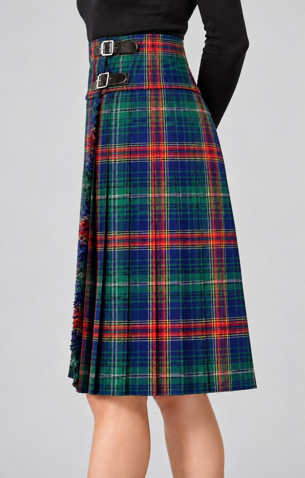 A high-waisted pleated kilt in a classic tartan plaid pattern of green, blue, red, and yellow, featuring a double-buckle waistband, shown on a model against a neutral gray background.