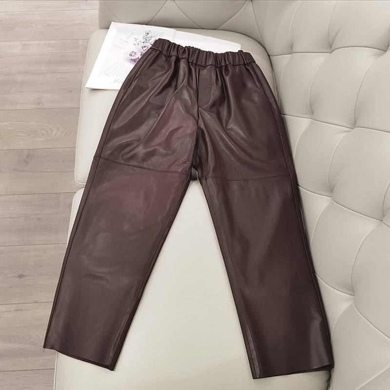 Brown leather pants on a white cushioned surface with a wooden floor background