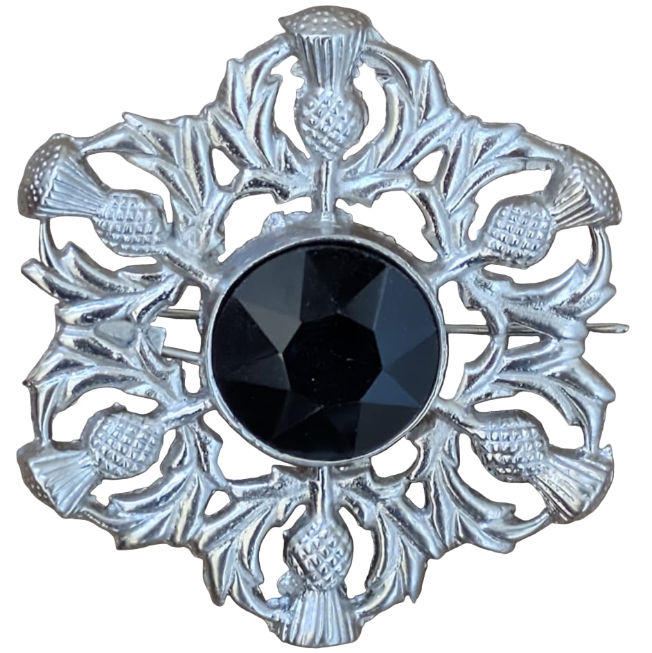 Decorative brooch with a black center and silver thistle design on a wooden surface