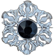 Decorative brooch with a black center and silver thistle design on a wooden surface