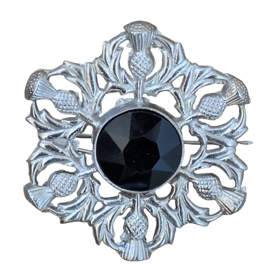 Decorative brooch with black center and silver intricate design on a wooden surface