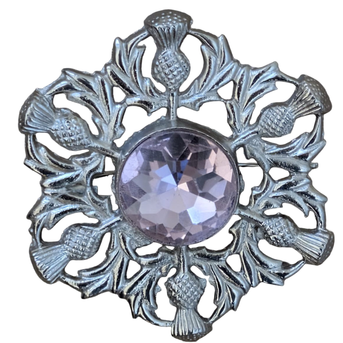 Decorative brooch with pink gemstone and thistle design on a wooden surface