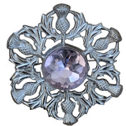Decorative brooch with pink gemstone and thistle design on a wooden surface