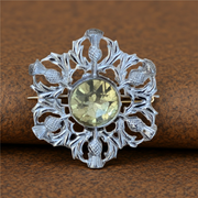 Decorative silver brooch with central gemstone on a brown background