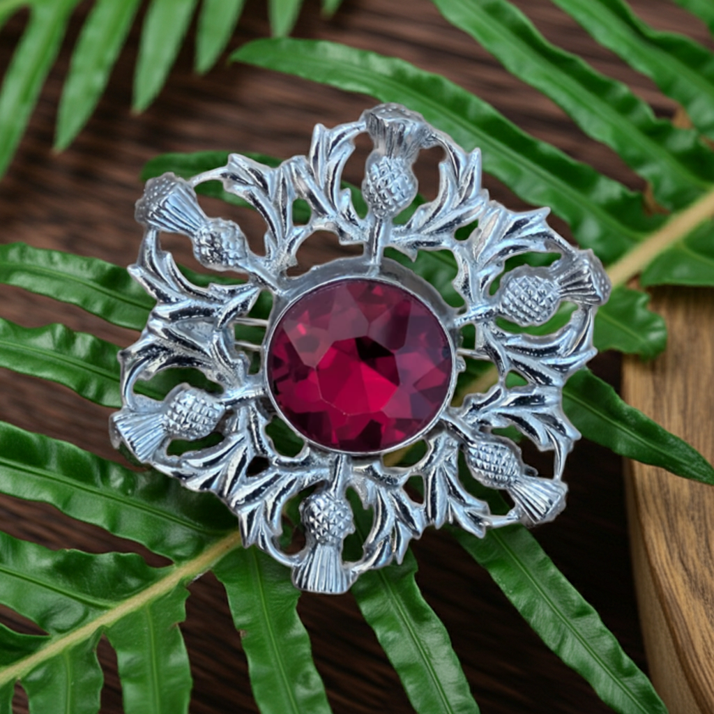 Silver brooch with a red gemstone on green leaves