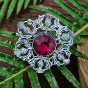 Silver brooch with a red gemstone on green leaves