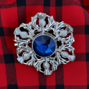 Decorative brooch with blue gemstone on a red and black checkered fabric background