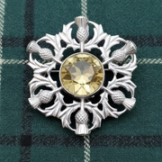 Silver brooch with a yellow gemstone on a green plaid fabric background